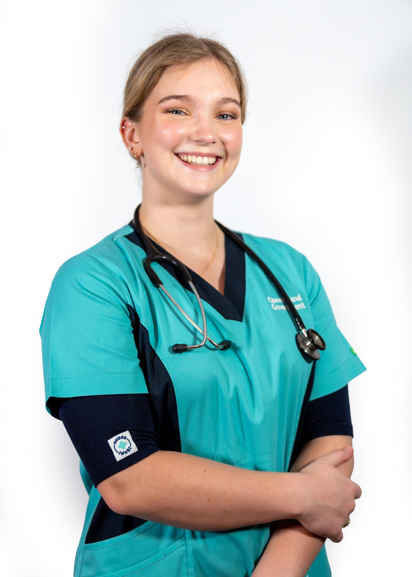 Happy, smiling young nurse wearing navy coloured Under Snugs under a bright teal healthcare work top & a stethoscope around her neck